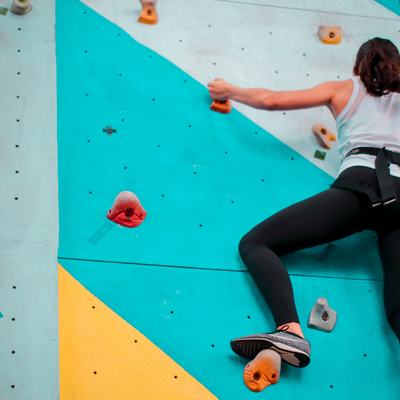 Eine Frau klettert an einer Kletterwand mit Sicherung.