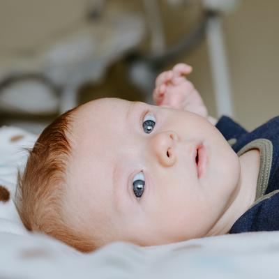 Ein Baby liegt auf dem Rücken. Es hat rötliche Haare und blaue Augen. Es schaut den Betrachter an.